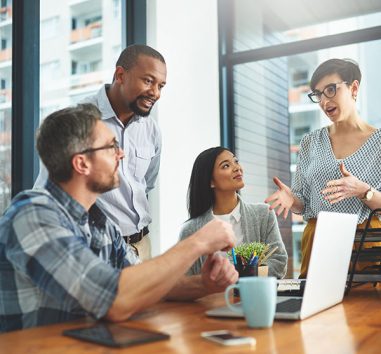 A group of employees having a discussion in front of a laptop in an office building downtown.